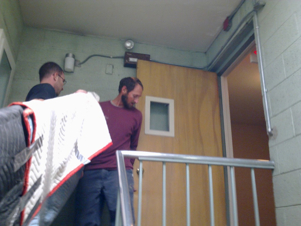 2 men carrying a tabletop up a narrow stairwell, at the top