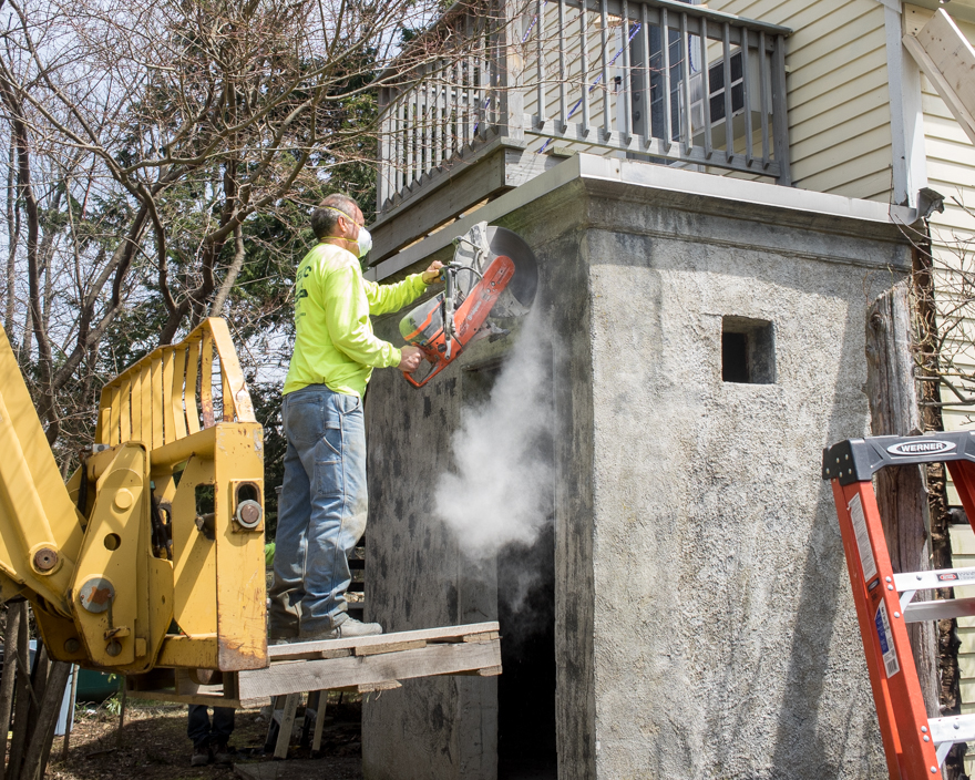 Man using concrete-cutting saw to make access hole in concrete wall