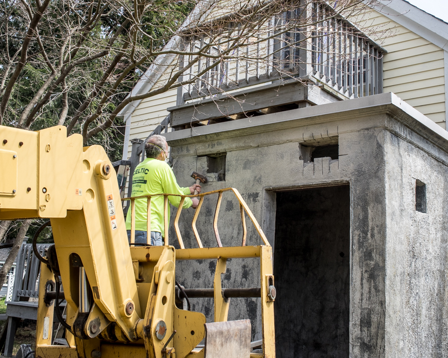 Man using sledgehammer to make access hole in concrete wall